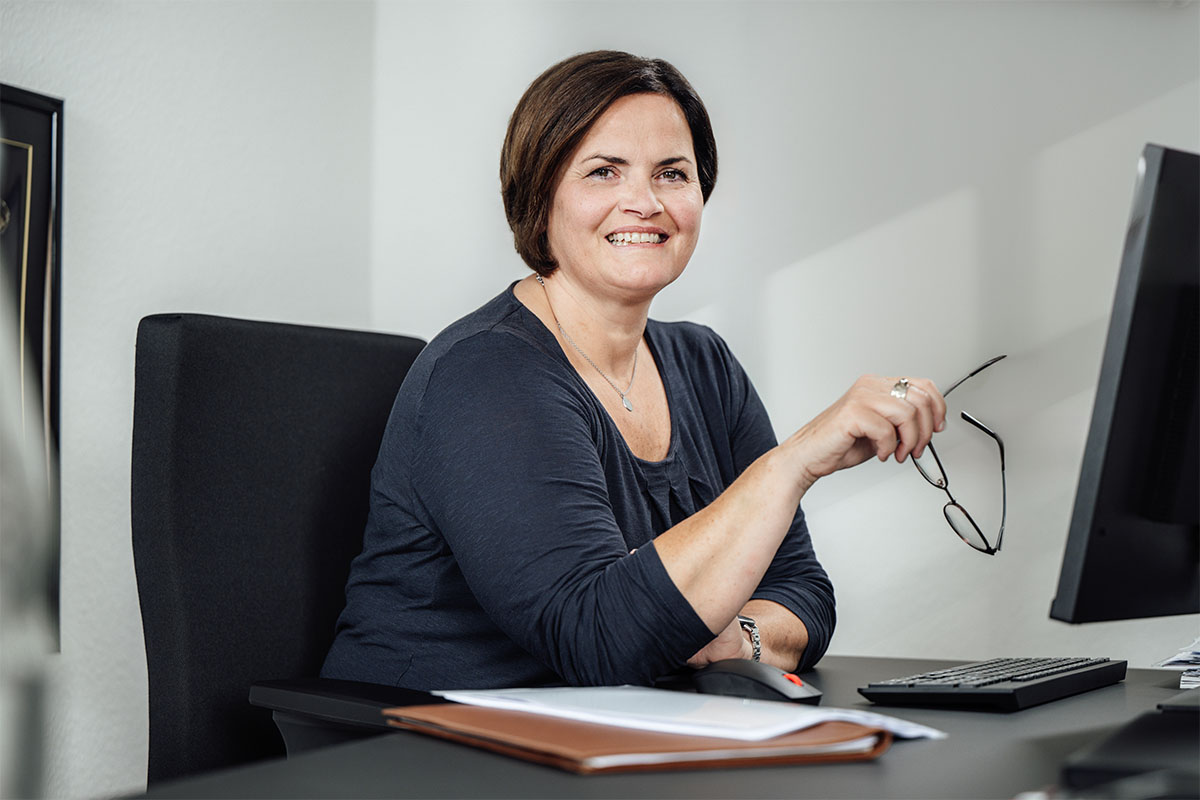 Smiling businesswoman working at a computer in an office, holding glasses and using a monitor