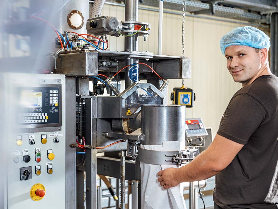 Technician operating industrial packaging machine in a factory with cleanroom hairnet and control panel