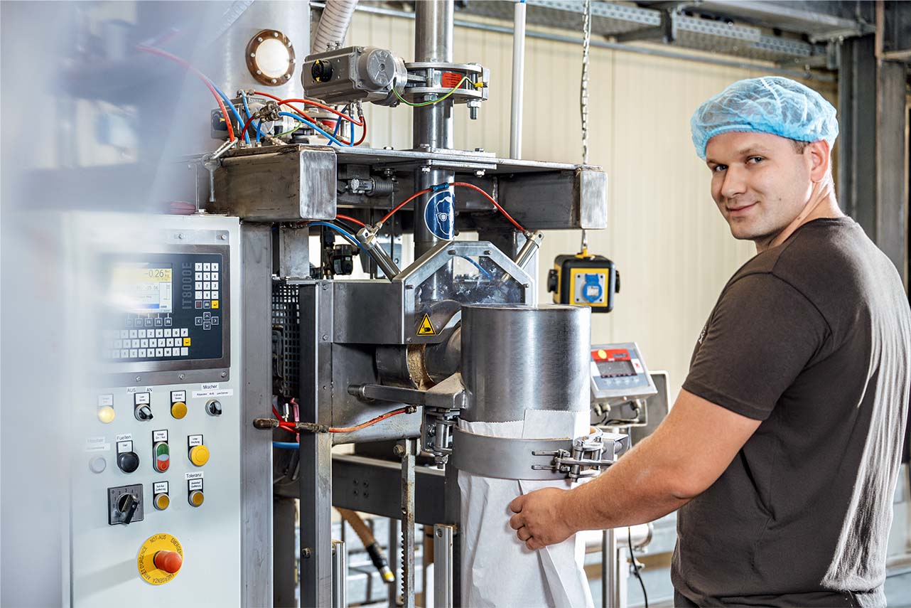 Technician operating industrial packaging machine in a factory with cleanroom hairnet and control panel