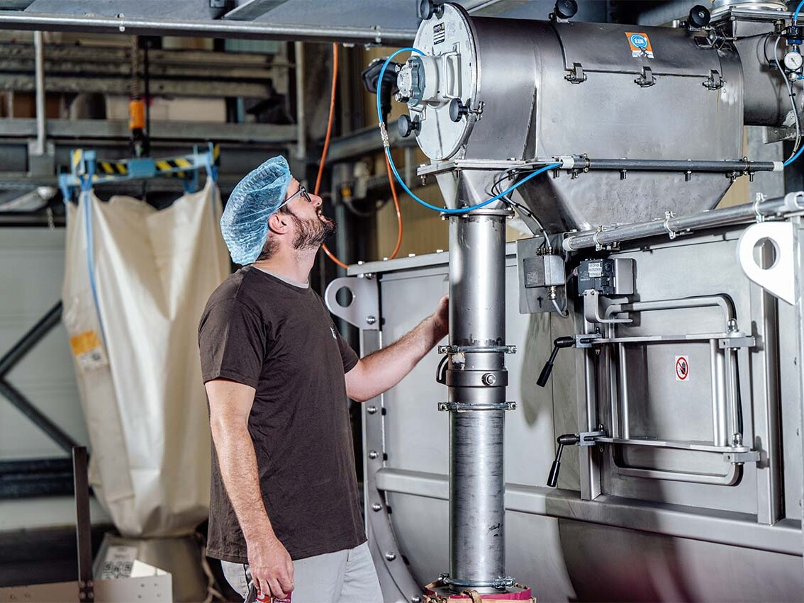 Technician inspecting industrial processing equipment with hoses and control panel in a manufacturing facility