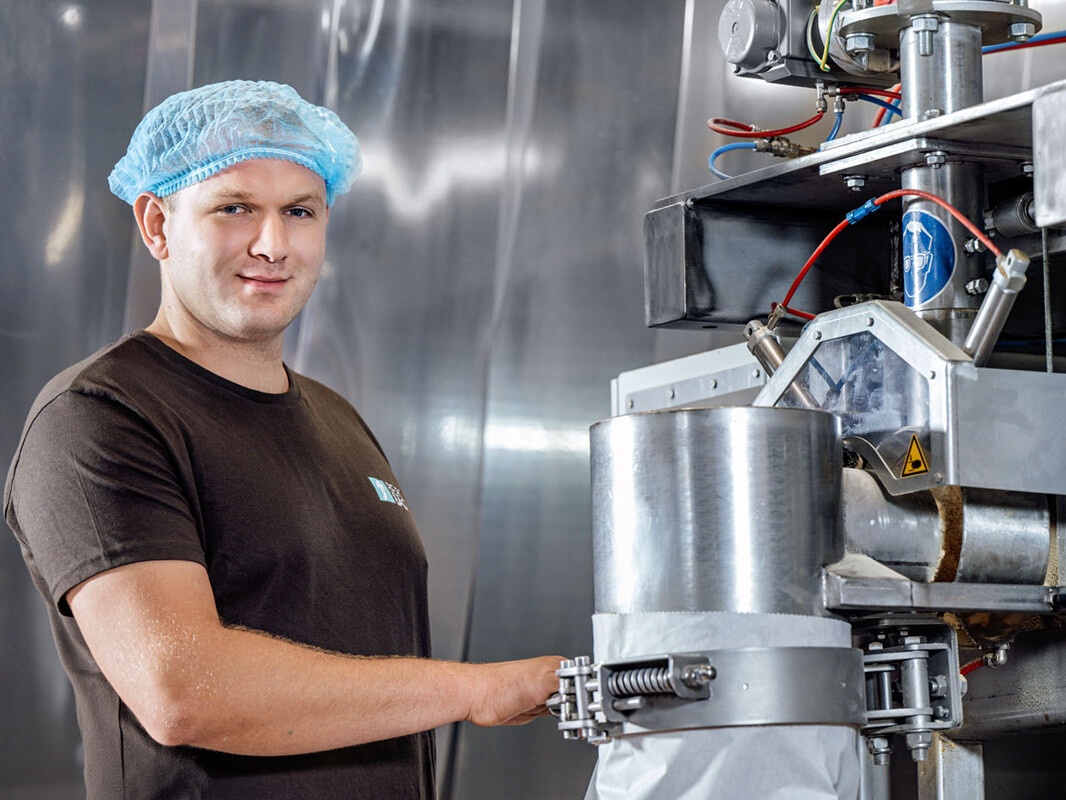 Food production worker in hairnet and lab attire operating stainless processing machinery in a hygienic facility
