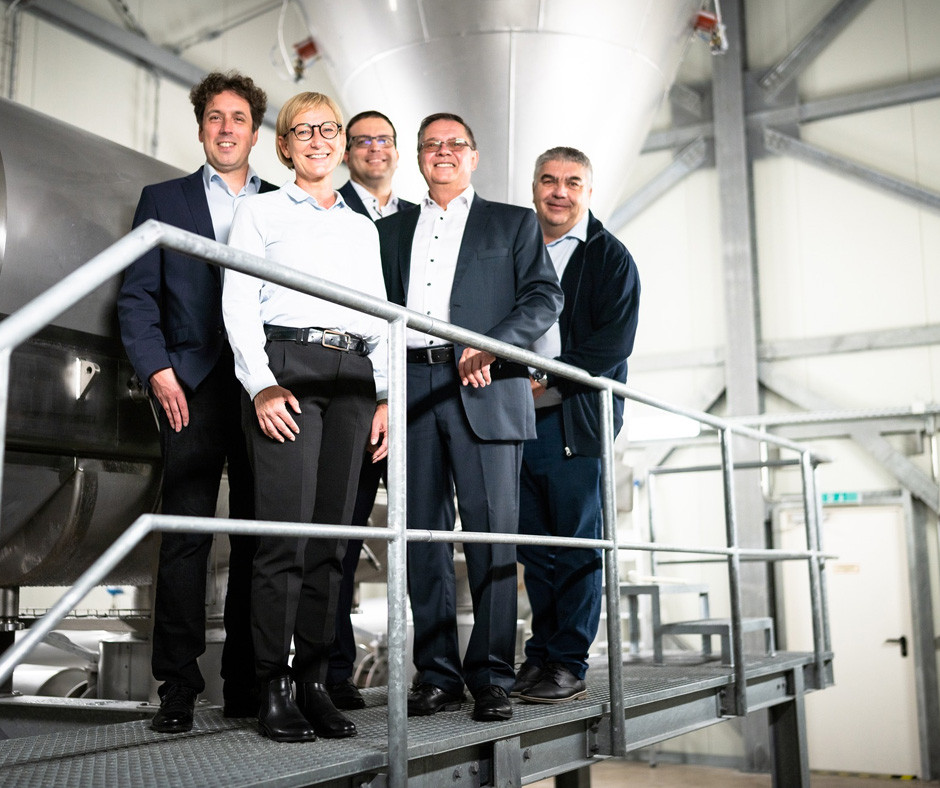 Business team posing in industrial facility with railings and modern equipment background
