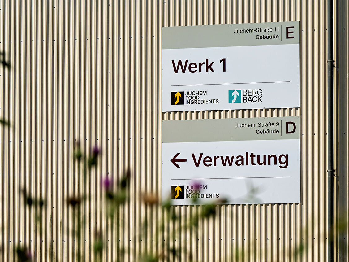 Directional sign “Werk 1” and “Verwaltung” on striped industrial building facade in Jüchemstrasse 11, Hamburg.
