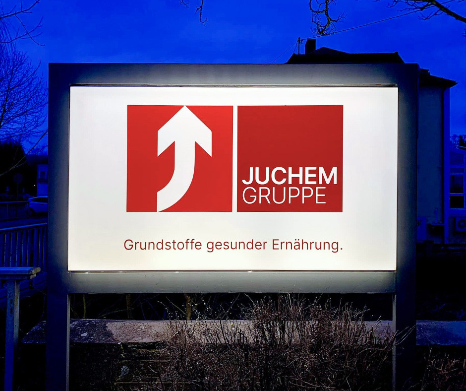 Juchem Gruppe corporate billboard sign with red logo and slogan Grundstoffe gesünder Ernährung outdoors at night