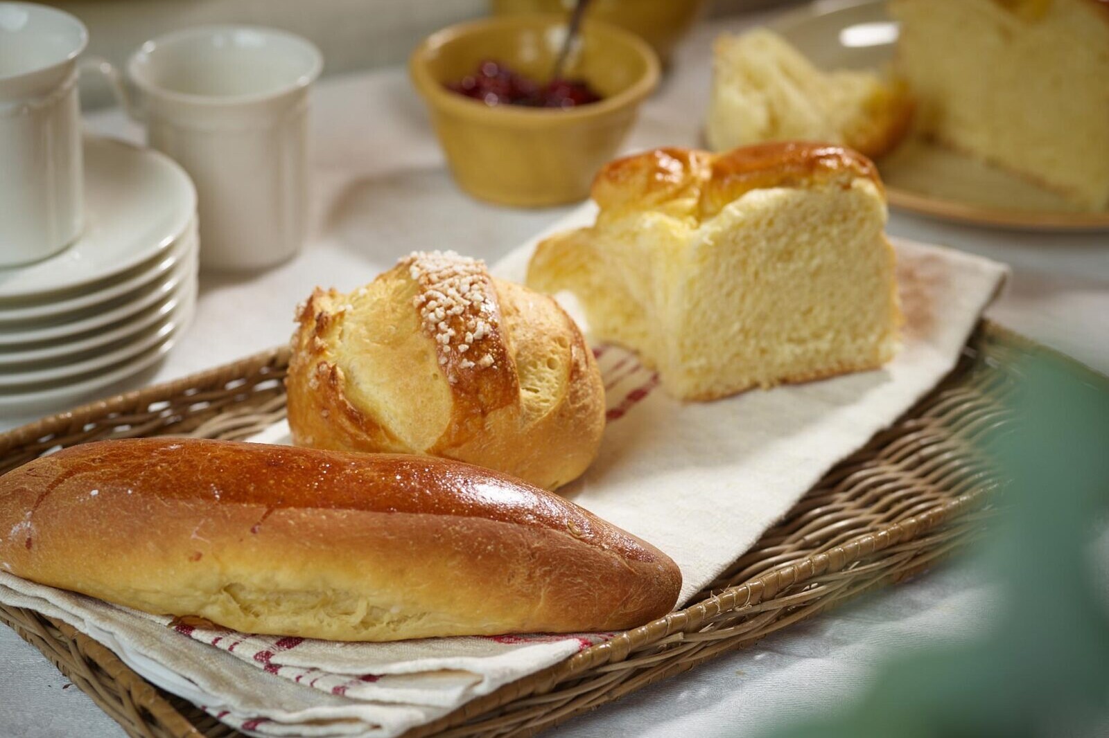 Fresh baked bread rolls and brioche on a serving basket with butter and fruit toppings in background
