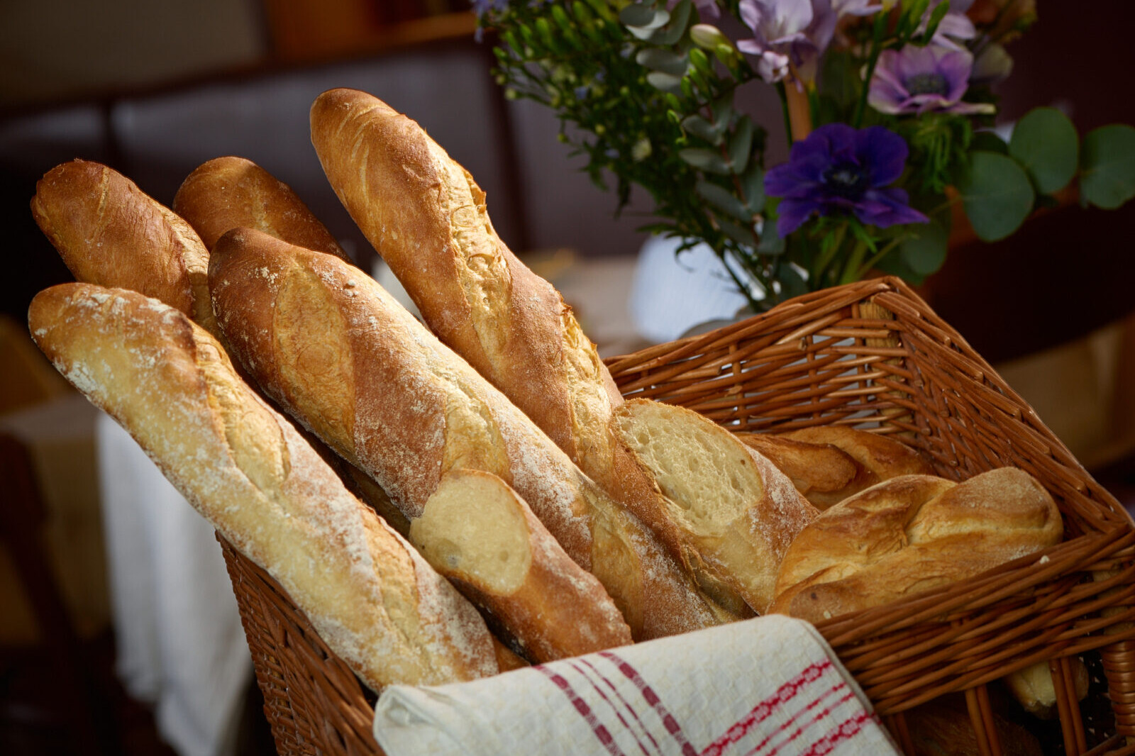 Fresh baguette loaves in a wicker basket with purple and green flowers background in warm light, bakery food photo