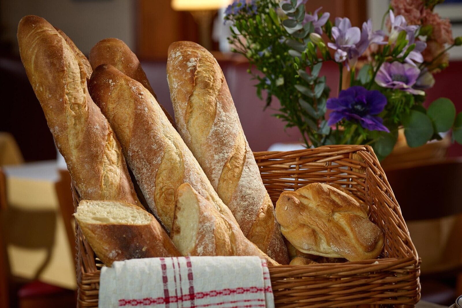 Fresh baguette loaves in a basket with a bouquet of colorful flowers in a cozy café setting