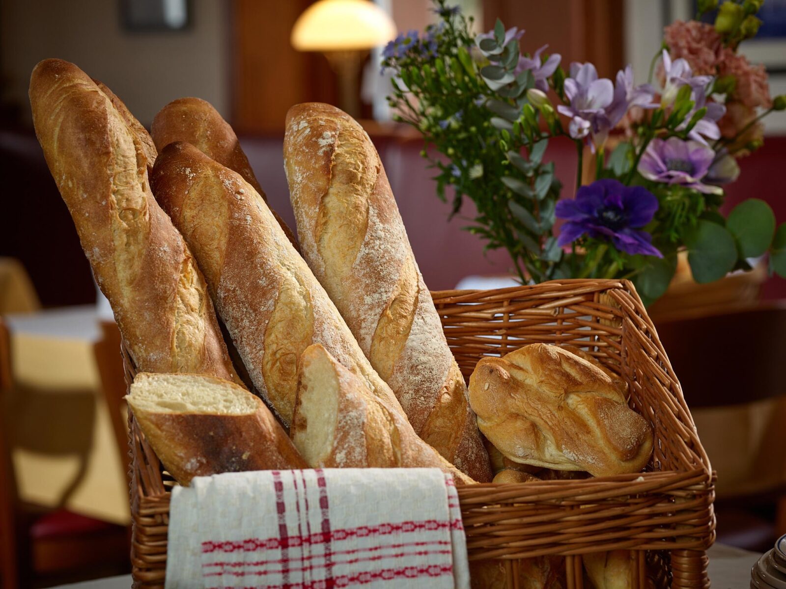 Fresh baguette loaves in a basket with a bouquet of colorful flowers in a cozy café setting