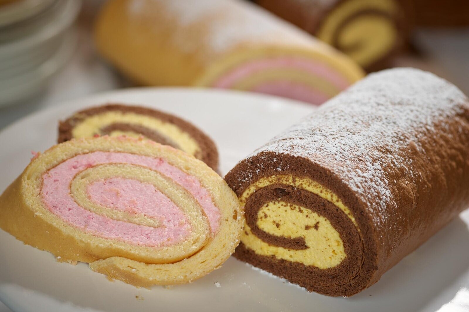 Assorted sliced swiss roll cake with pink and chocolate swirls dusted with powdered sugar on a plate