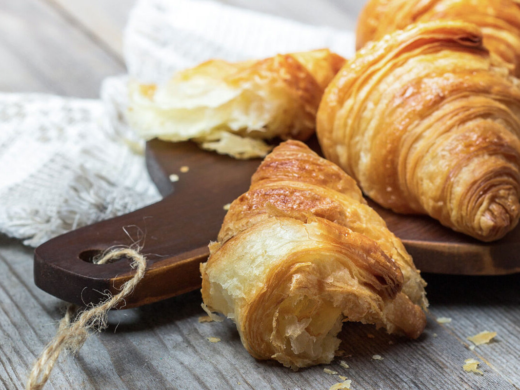 Freshly baked croissants on a wooden board with a rustic cloth background, highlighting their flaky texture.