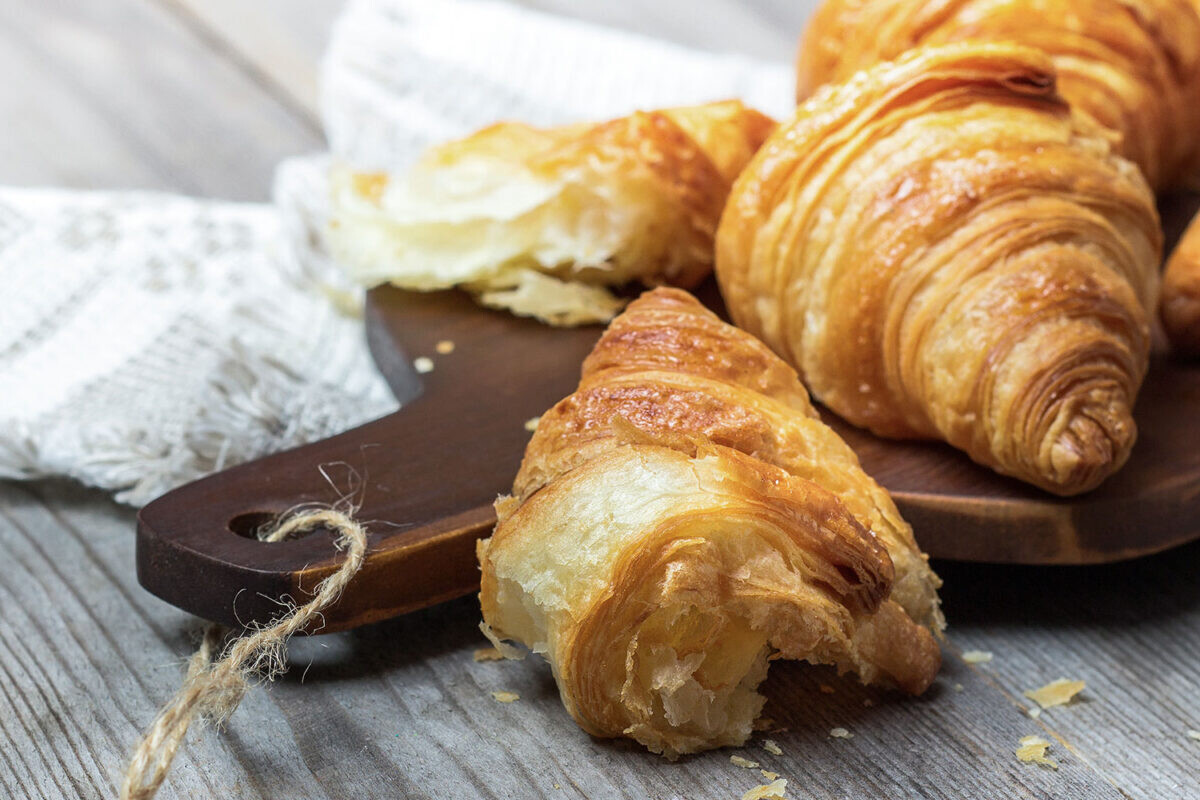 Freshly baked croissants on a wooden board with a rustic cloth background, highlighting their flaky texture.