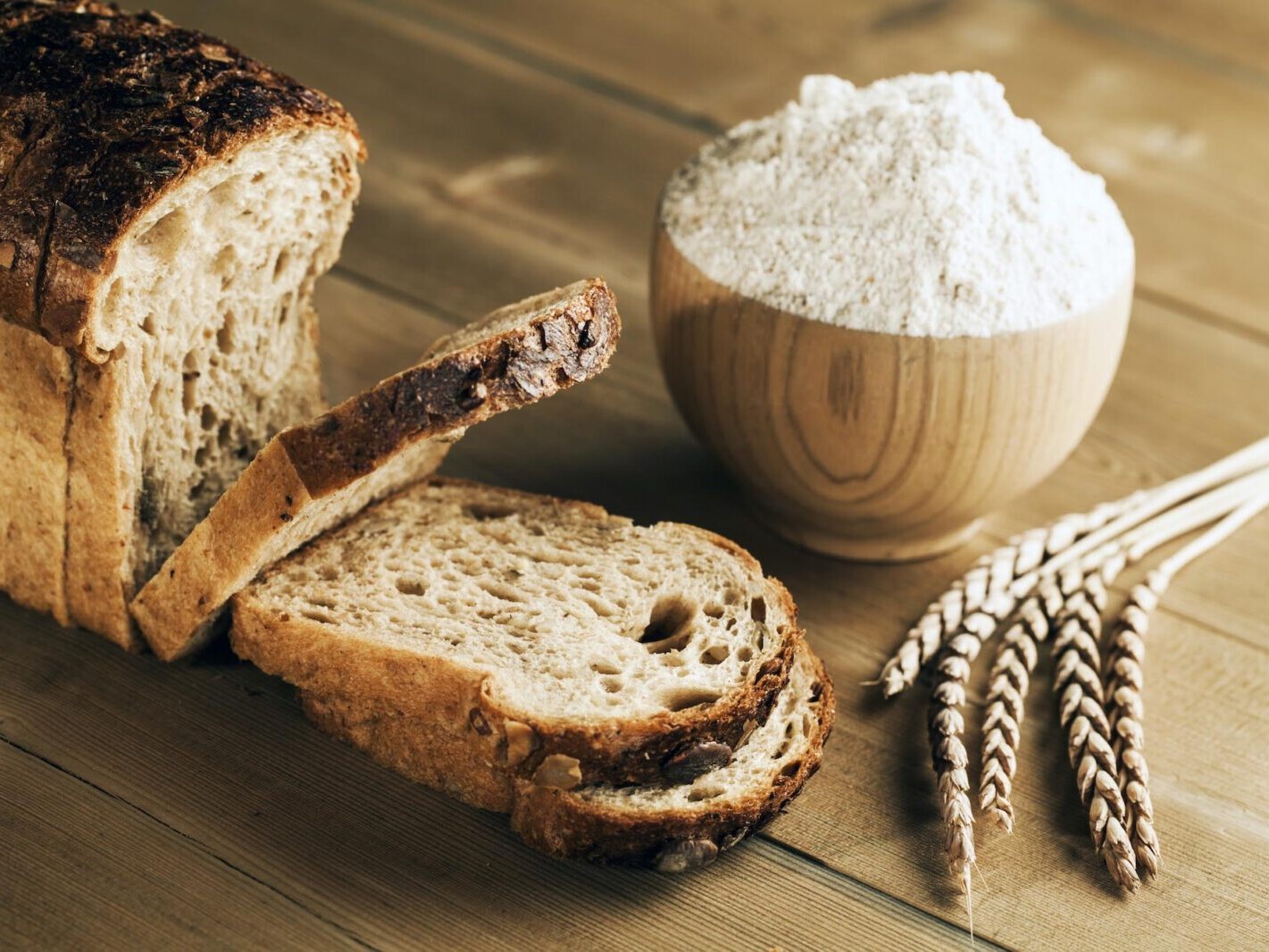 Rustic sliced sourdough bread with wooden bowl and wheat stalks on a wooden table