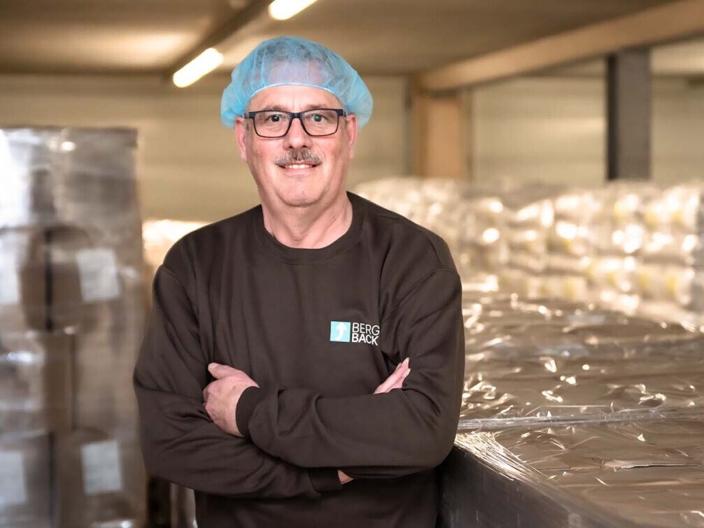 Male chef wearing hairnet and glasses standing in a food processing facility, arms crossed, Berg Back workwear.
