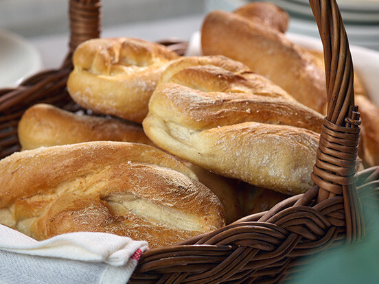 Freshly baked baguette rolls in a wicker basket with warm golden crust.