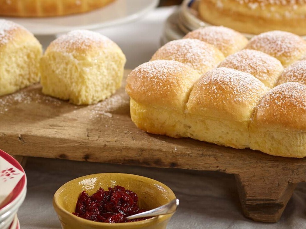 Fresh baked Brazilian pão de queijo rolls dusted with powdered sugar on a wooden serving board with jam dip