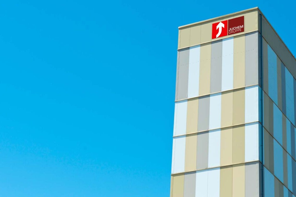 Modern JUCHEM GRUPPE office building facade against a clear blue sky with logo on top.