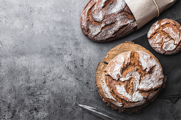 Rustic sourdough bread loaf and rolls with flour on parchment, rustic knife on dark background, copy space