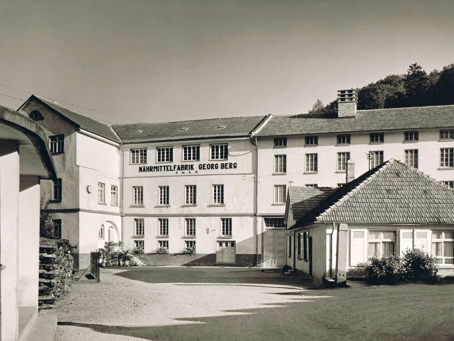 Historic factory building façade with sign “Nährmittel­fabrik Georg Berg” and tiled roofs, vintage campus exterior