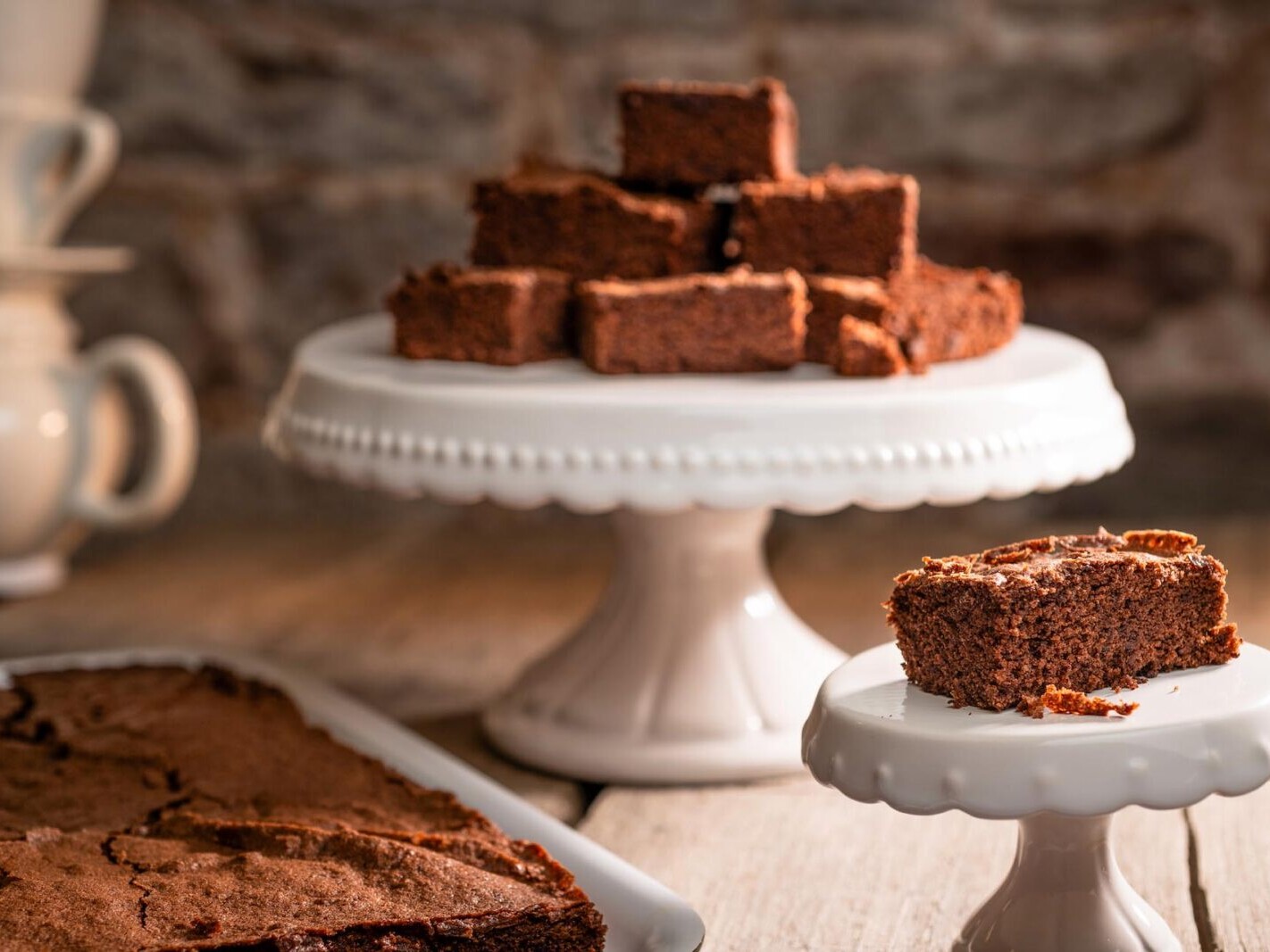 Chocolate brownies on white cake stands with cocoa-dusted rustic background, close-up dessert serving.