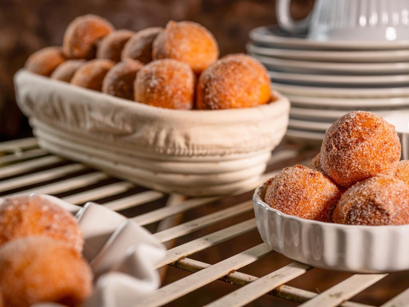 Freshly baked cinnamon sugar donuts on cooling racks with a bowl of golden pastries in the foreground