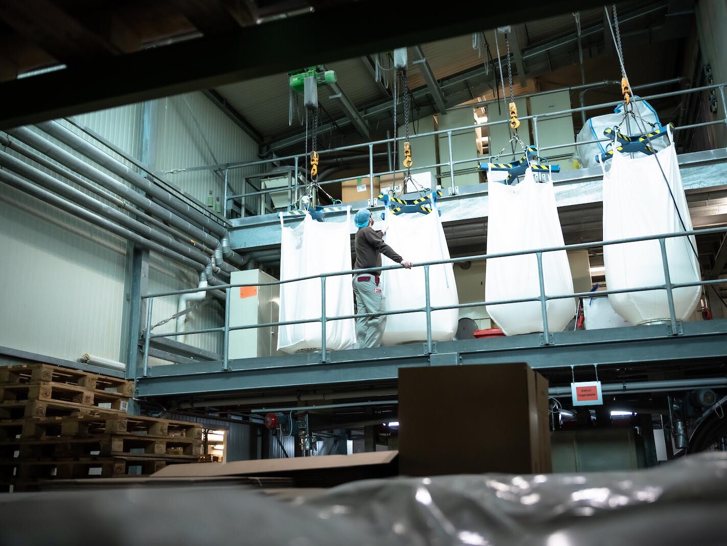 Worker manages large industrial bags on a metal platform in a warehouse setting.