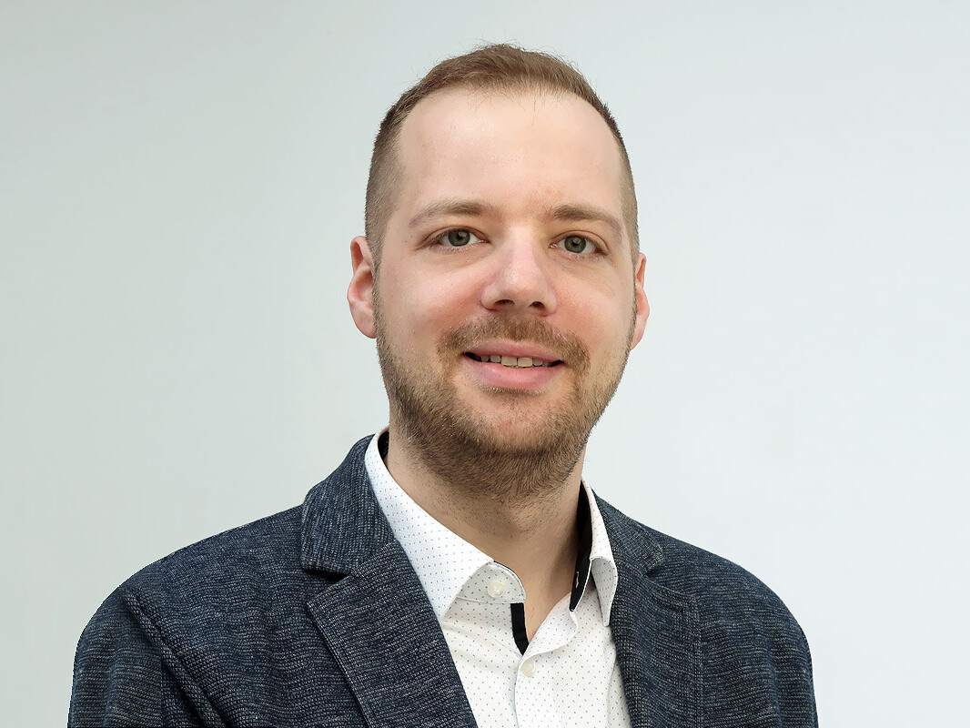 Portrait of a smiling man in a blazer and white shirt against a plain background, looking confident and approachable.